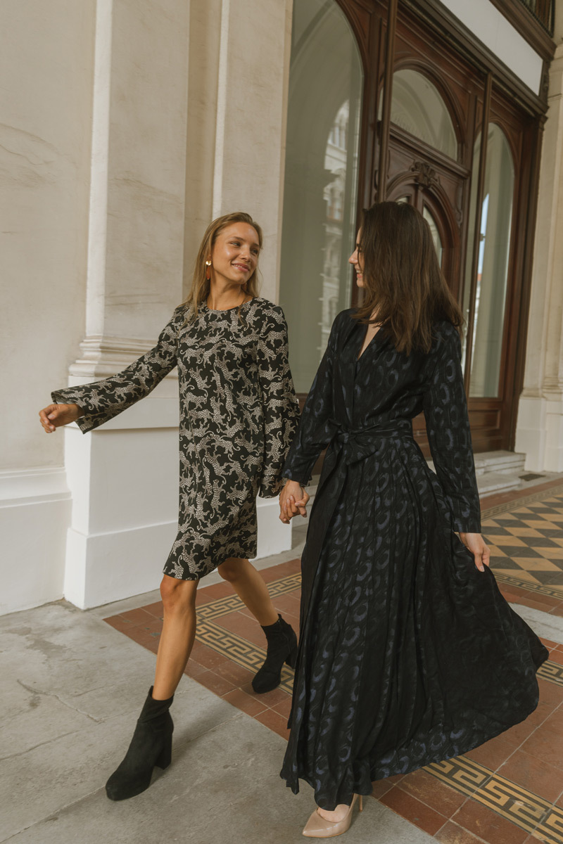 Two girls wearing long dresses, holding hands and walking surrounded by historic buildings