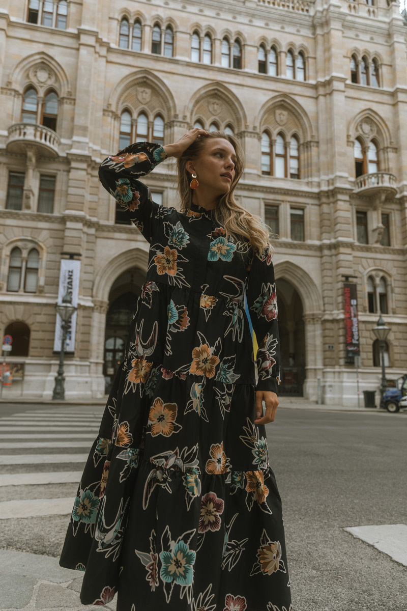 Blonde girl wearing a long dress, standing in front of a historic building