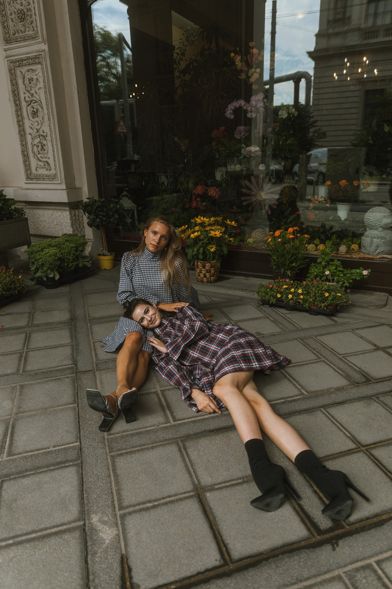 Two girls sitting on the floor in front of a flowers stand, wearing dresses