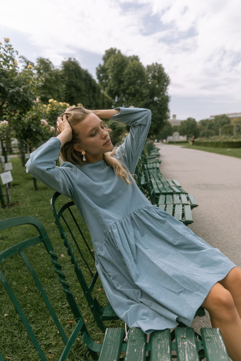 Blonde girl in a blue dress, sitting on a chair in a park