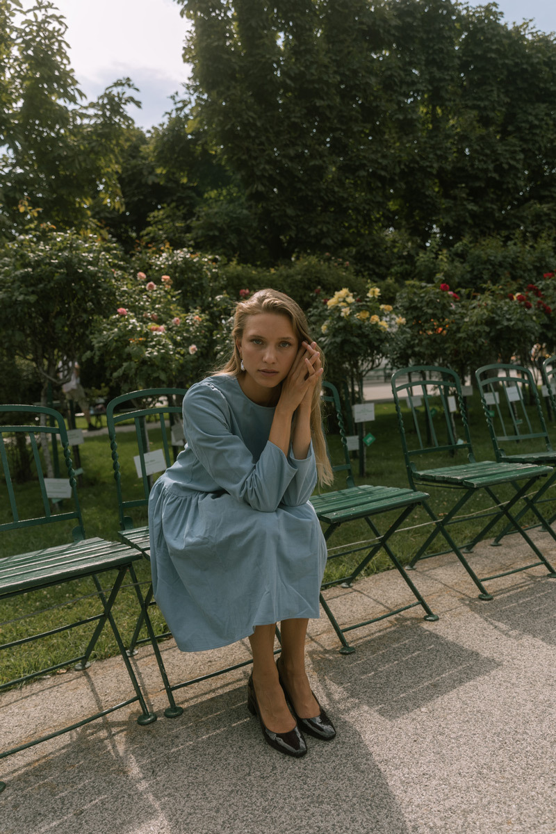 Blonde girl in a blue dress, sitting on a chair in a park