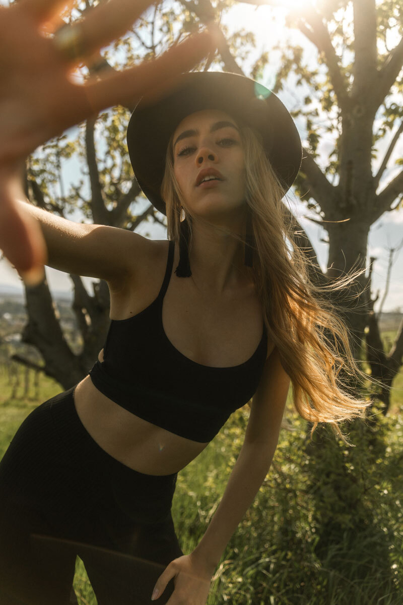 Blonde girl wearing a black outfit and black hat, standing in nature