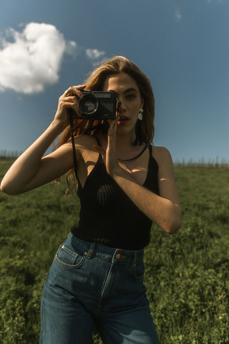 Girl standing on a field with an old analogue camera