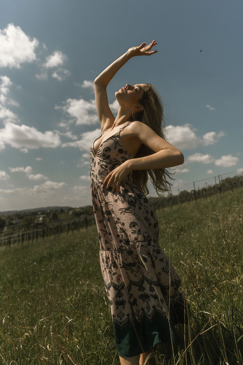 Girl standing in nature, with closed eyes and the arms stretched in the air