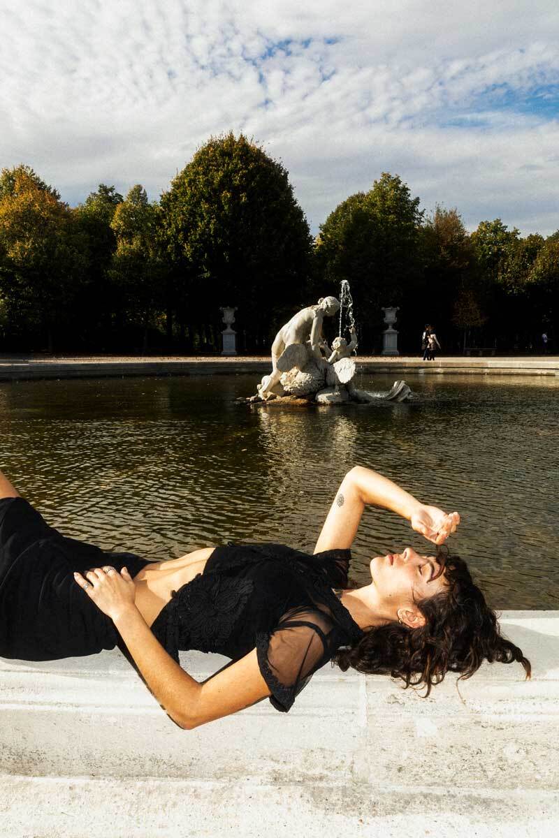 girl with brown hair laying on a fountain, holding hand in the air