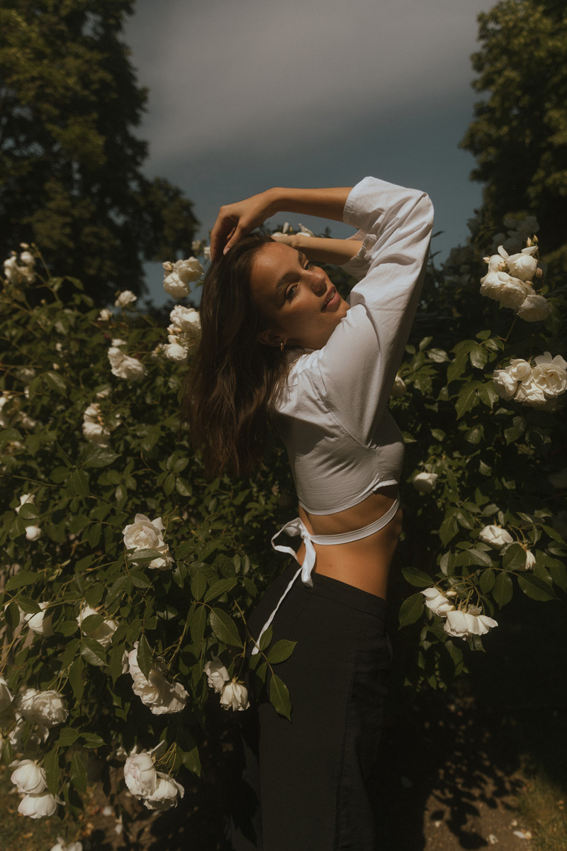 A girl in a white top standing in front of white roses