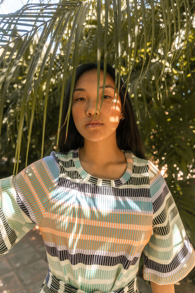 Girl standing in front of palm leaf.