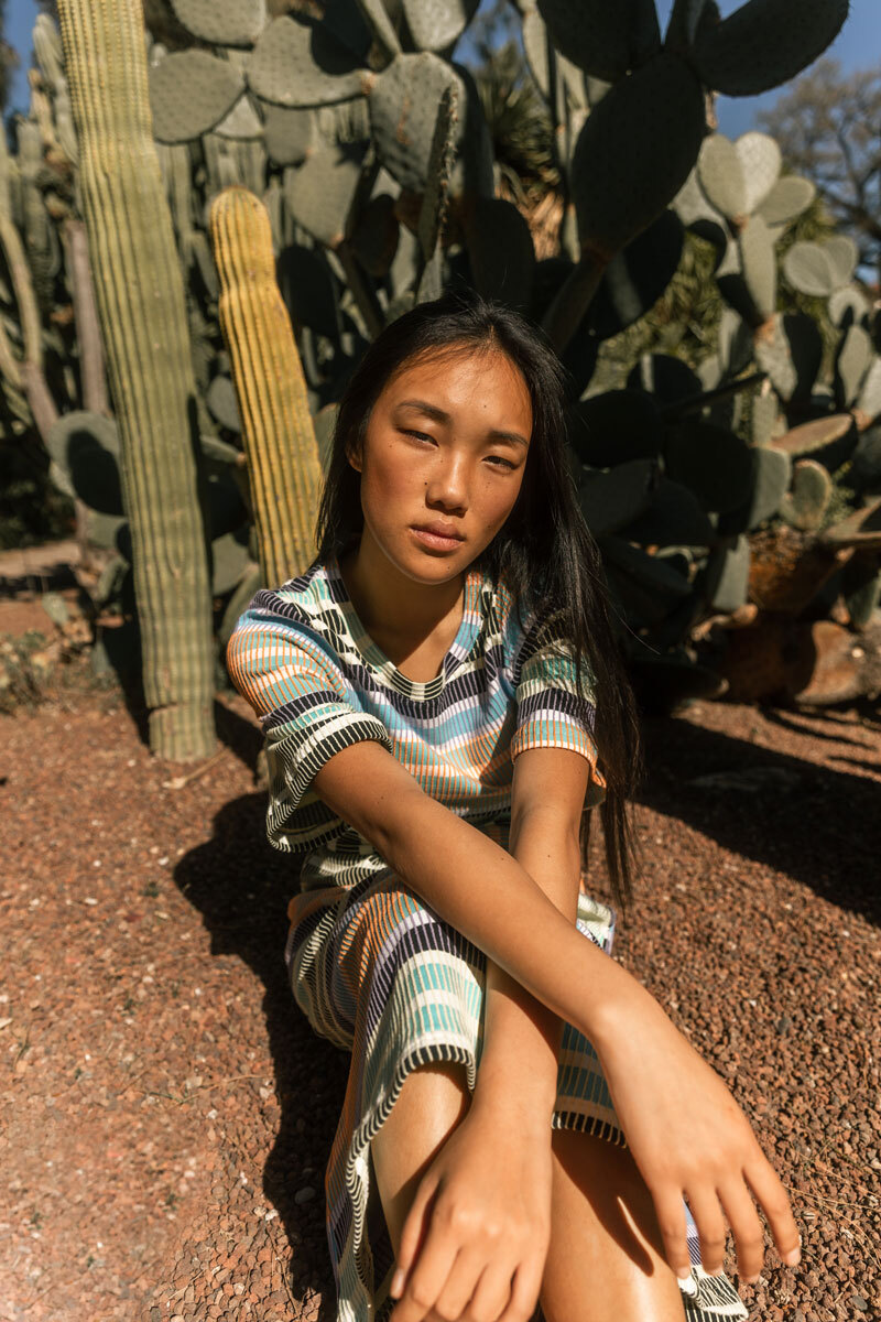 Girl sitting next to a cactus.