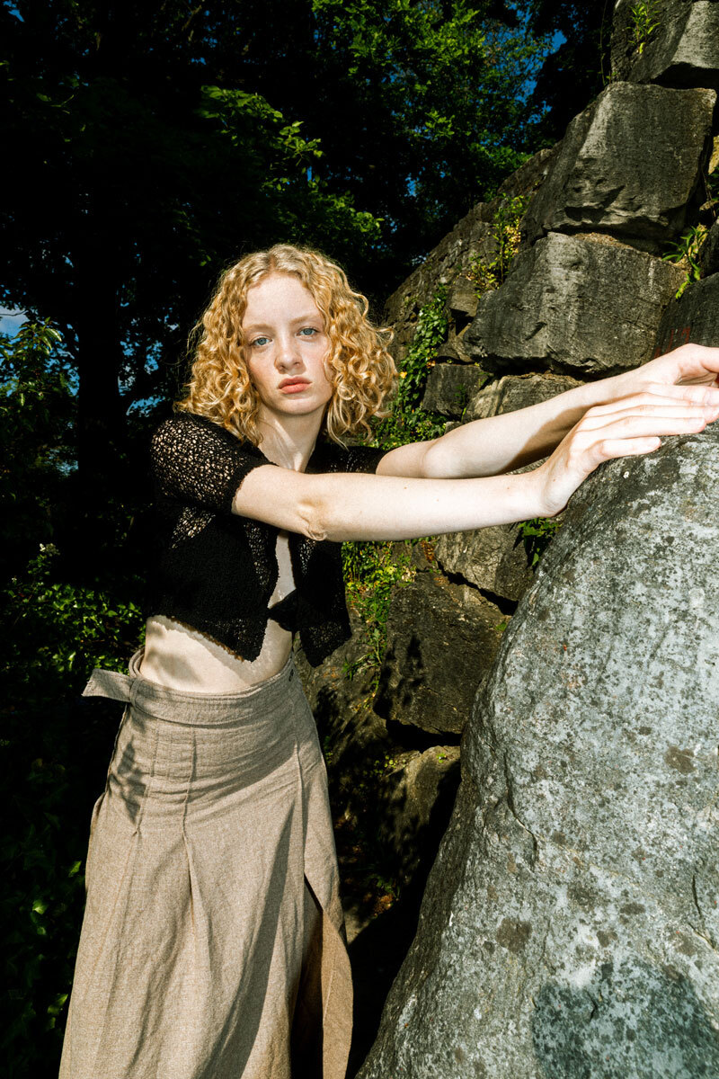 blonde girl standing next to a brock, wearing a skirt