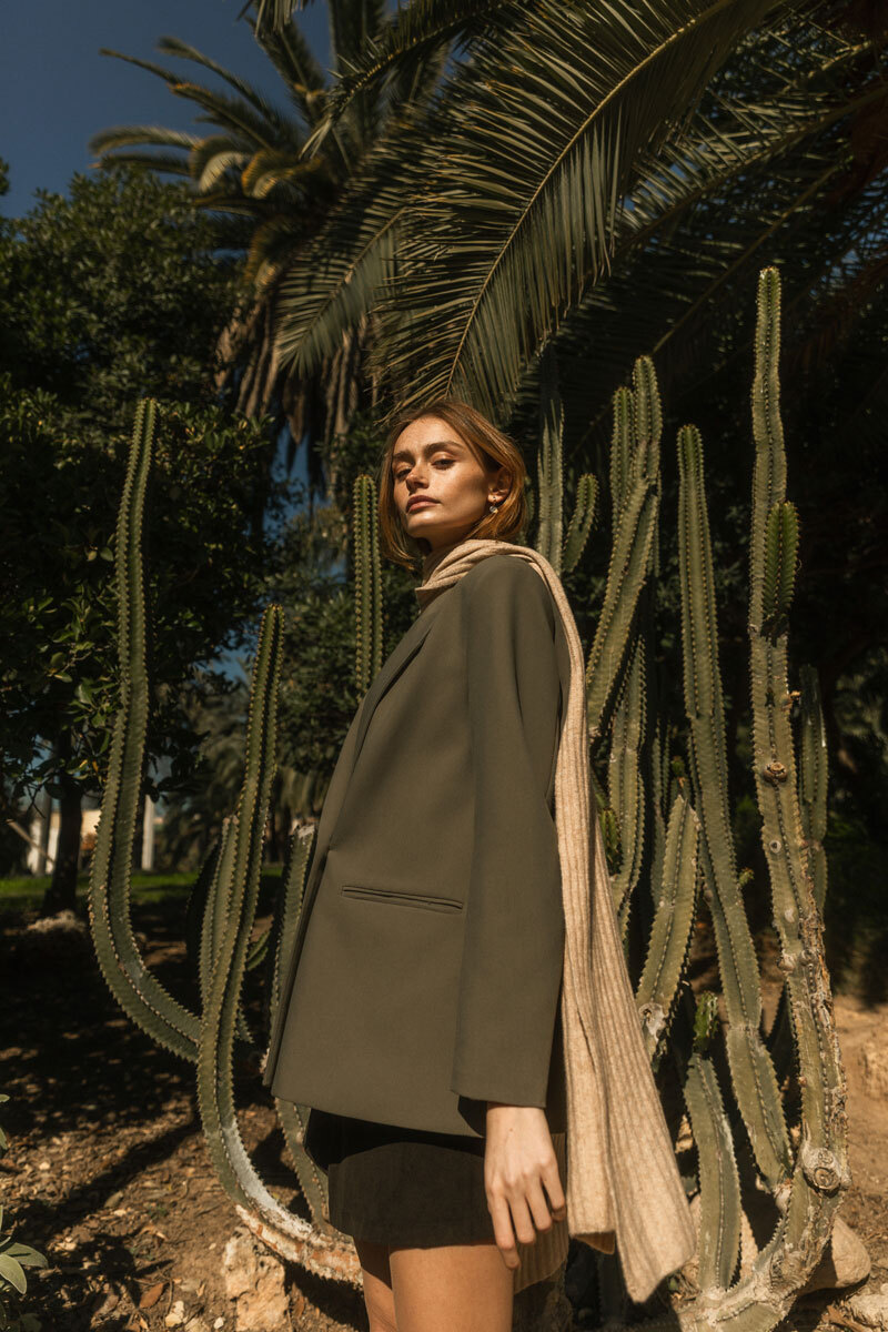 A blonde girl with a scarf standing in front of a cactus