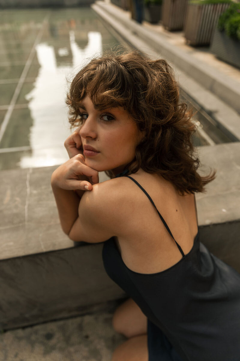 Girl leaning onto a fountain, looking back over her shoulder