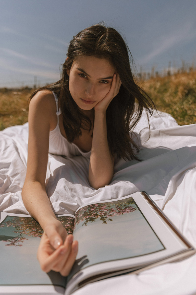 Girl laying on a blanket in the vineyards and reading a magazine