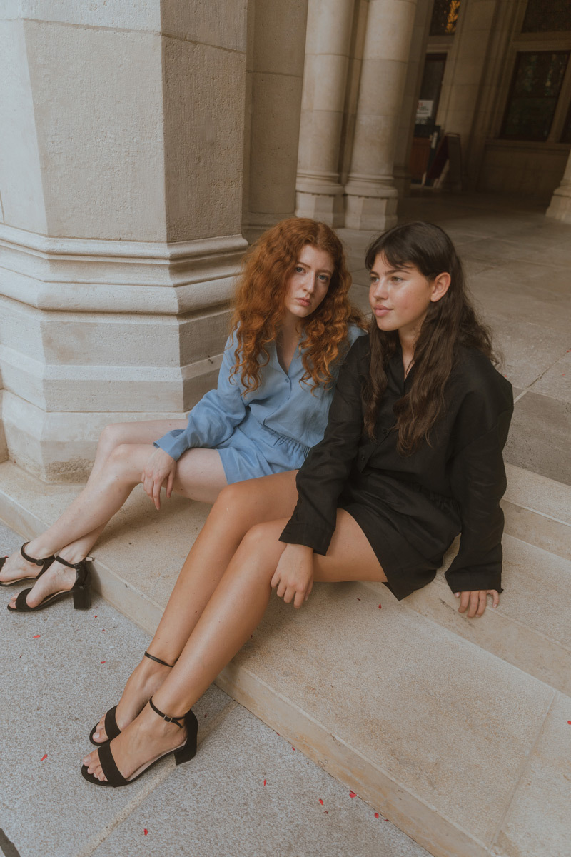 Two girls sitting on stairs. One girl is looking into the camera, the other is looking away