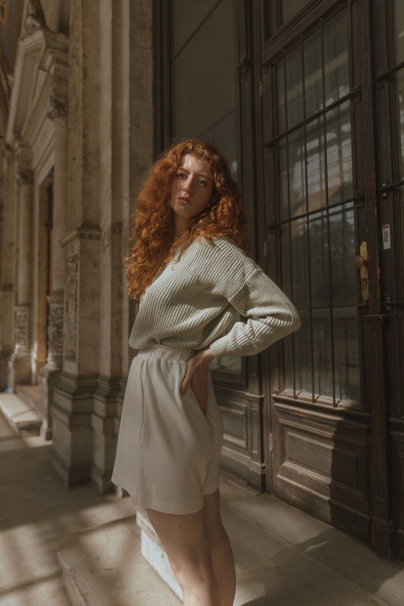 Girl with orange hair, wearing a green sweater is standing in front of an old door