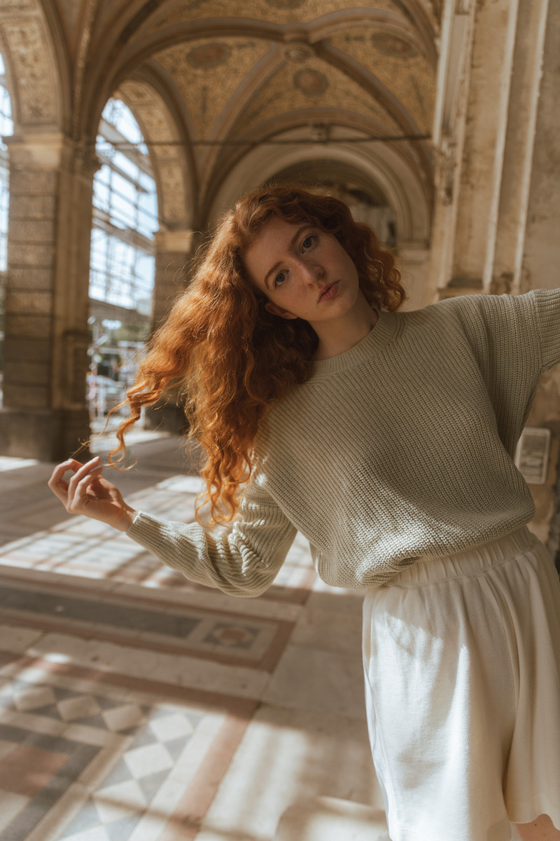 Girl with orange hair, wearing a green sweater and going through her hair with her hands