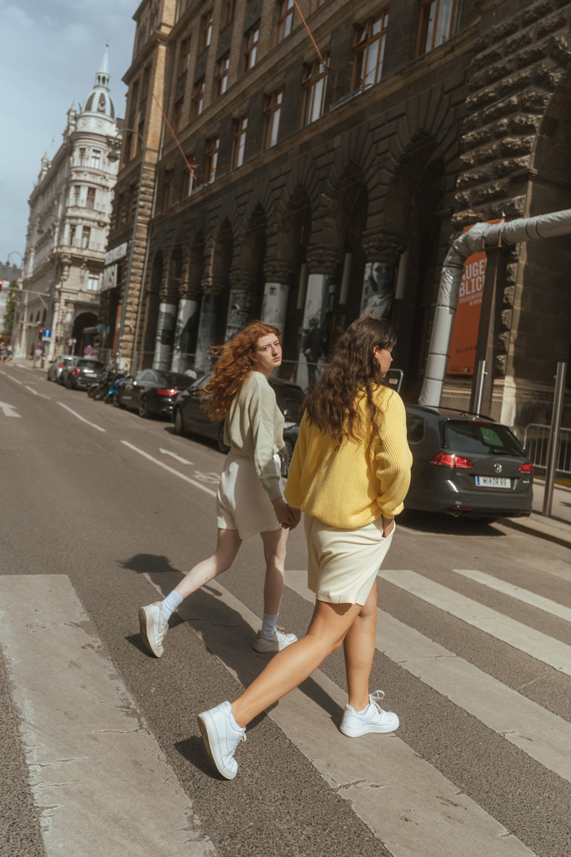 Two girls crossing the street. One girl is looking back into the camera